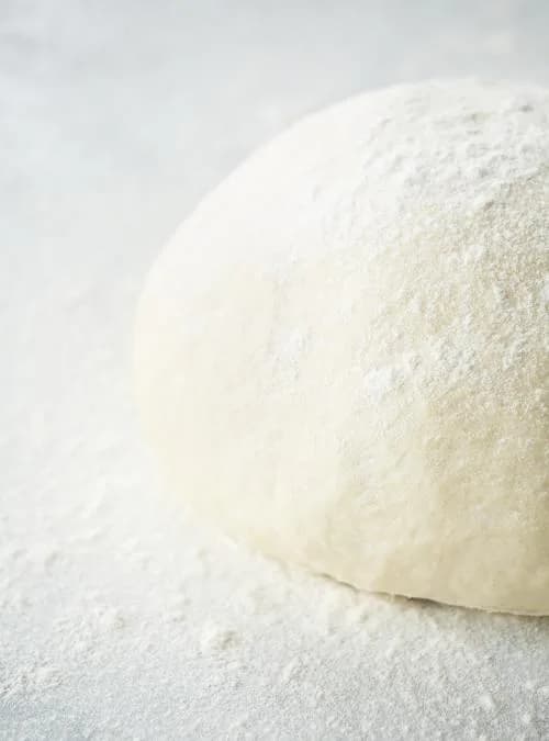 A ball of Tony's pizza dough on the bench, floured and ready to stretch