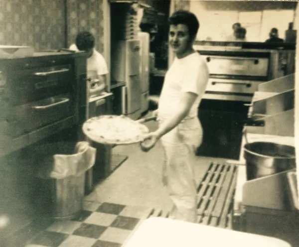 A pizzaiolo sliding a pie into the oven in Tony's early years