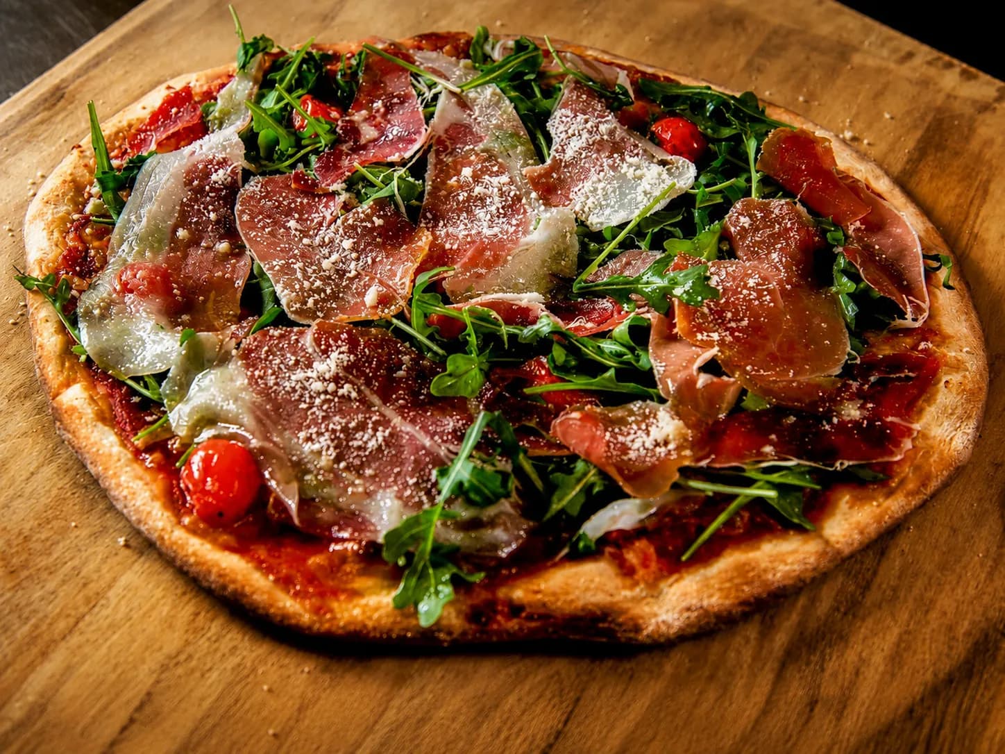 A pizza with prosciutto, fresh arugula, cherry tomatoes and parmesan