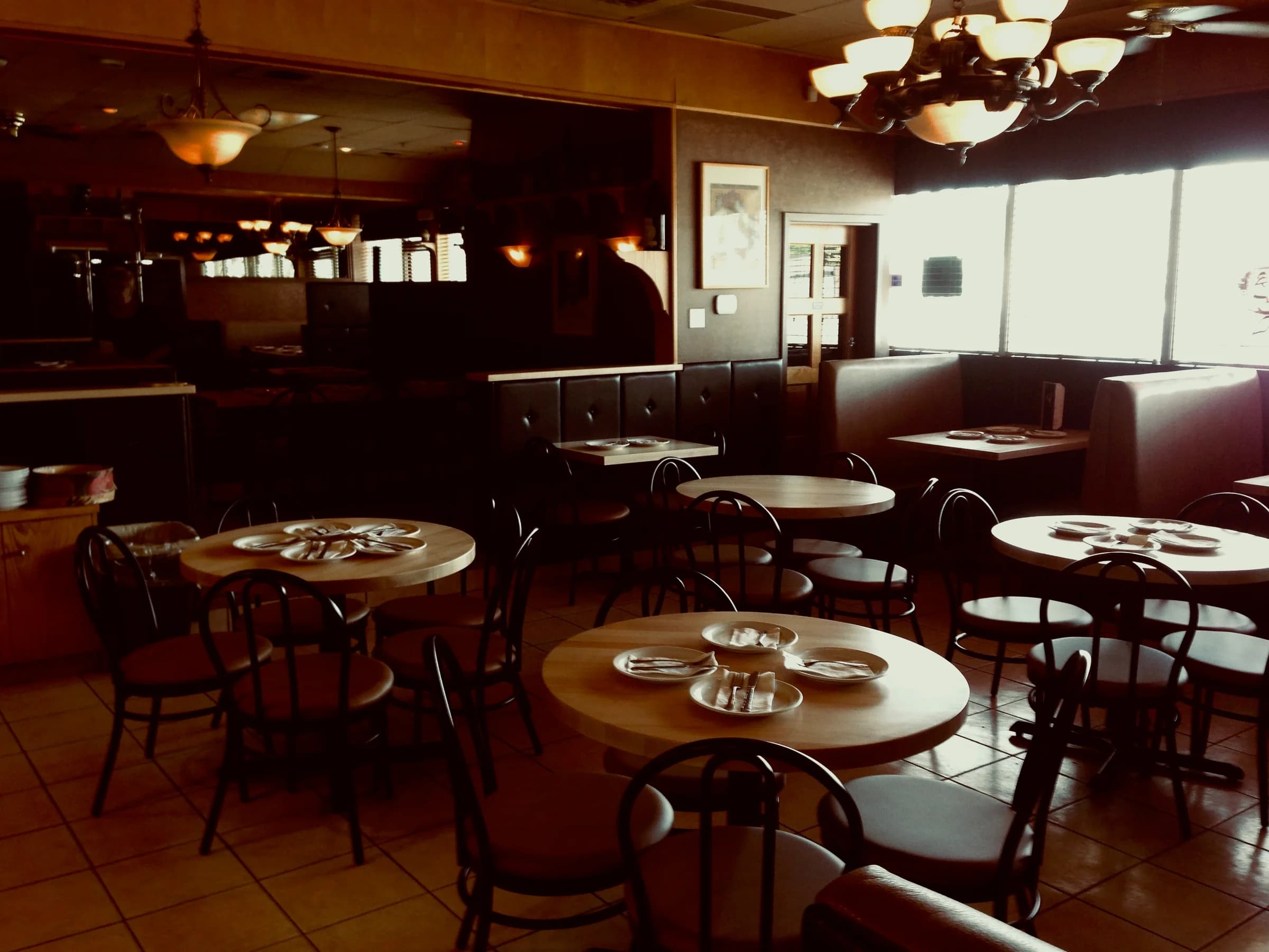 The dining room at Tony's, warm lighting over dark booths and round wooden tables set before service